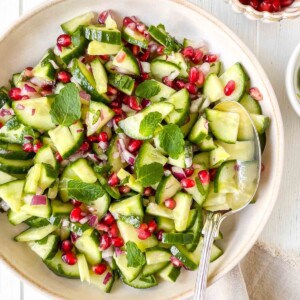 cucumber pomegranate salad in a cream bowl with a spoon.
