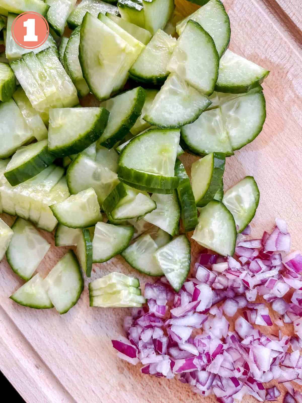 diced English cucumber and red onion on a wooden chopping board labelled number one.