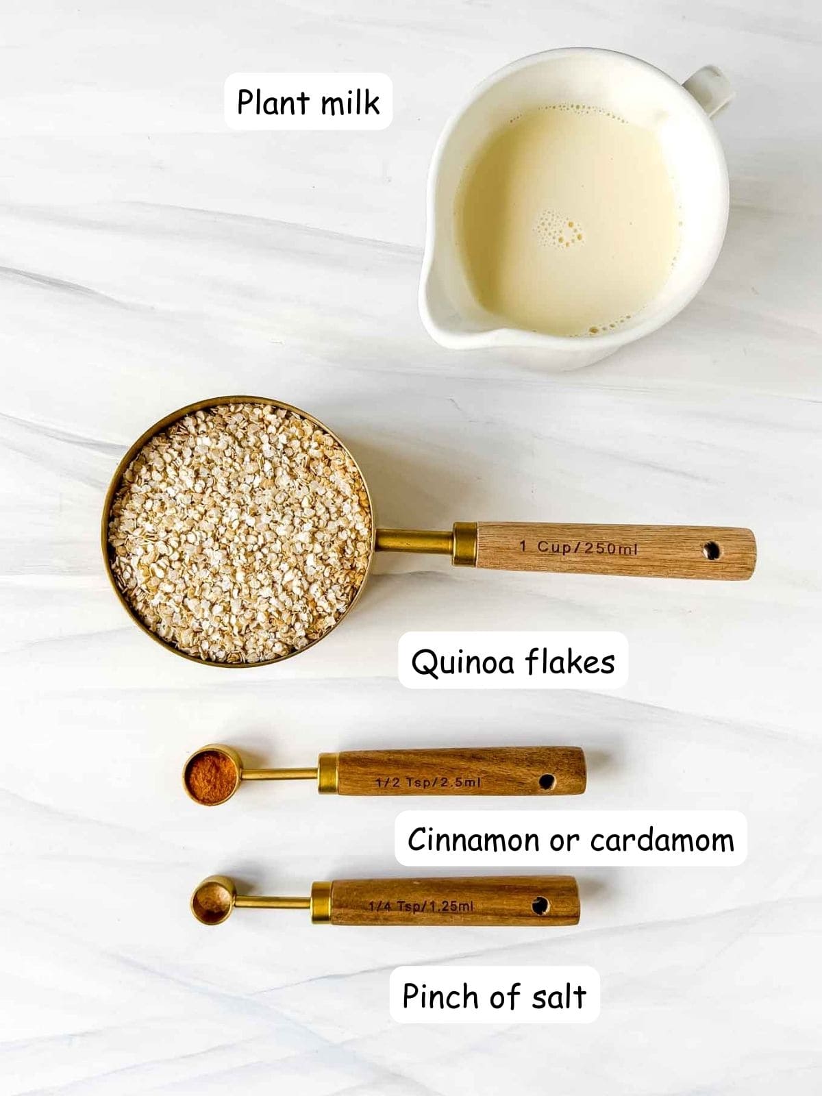 individually labelled ingredients to make quinoa flake porridge including a jug of plant milk and spoonful of cinnamon.