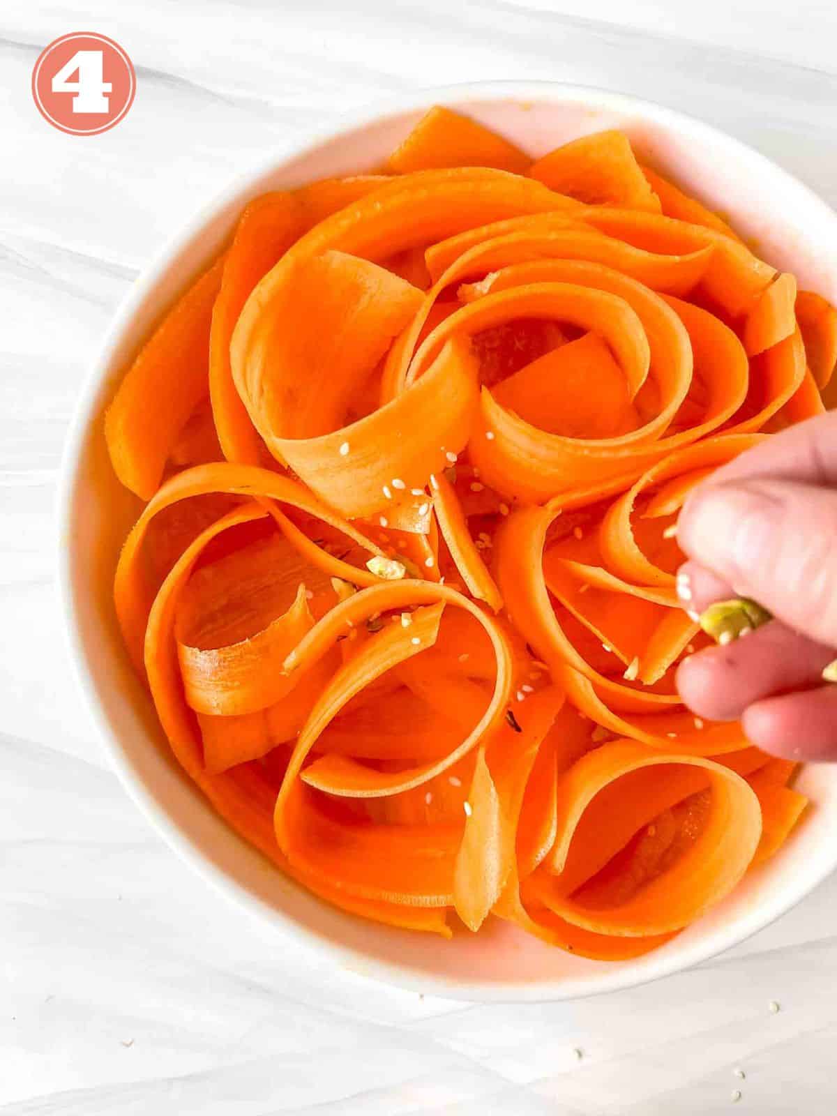 shaved carrots in a white bowl being sprinkled with seeds labelled number four.