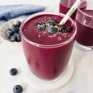 berry kale smoothie in three glasses next to a bowl of fresh blueberries.