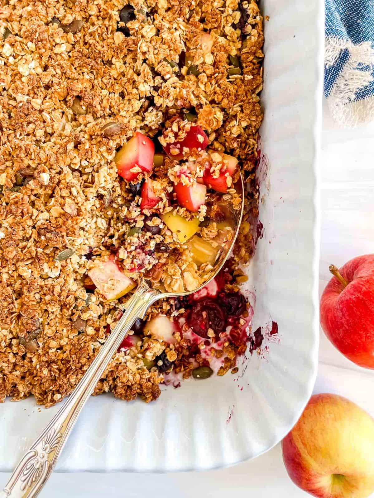 apple blueberry crisp in a baking pan next to red apples.