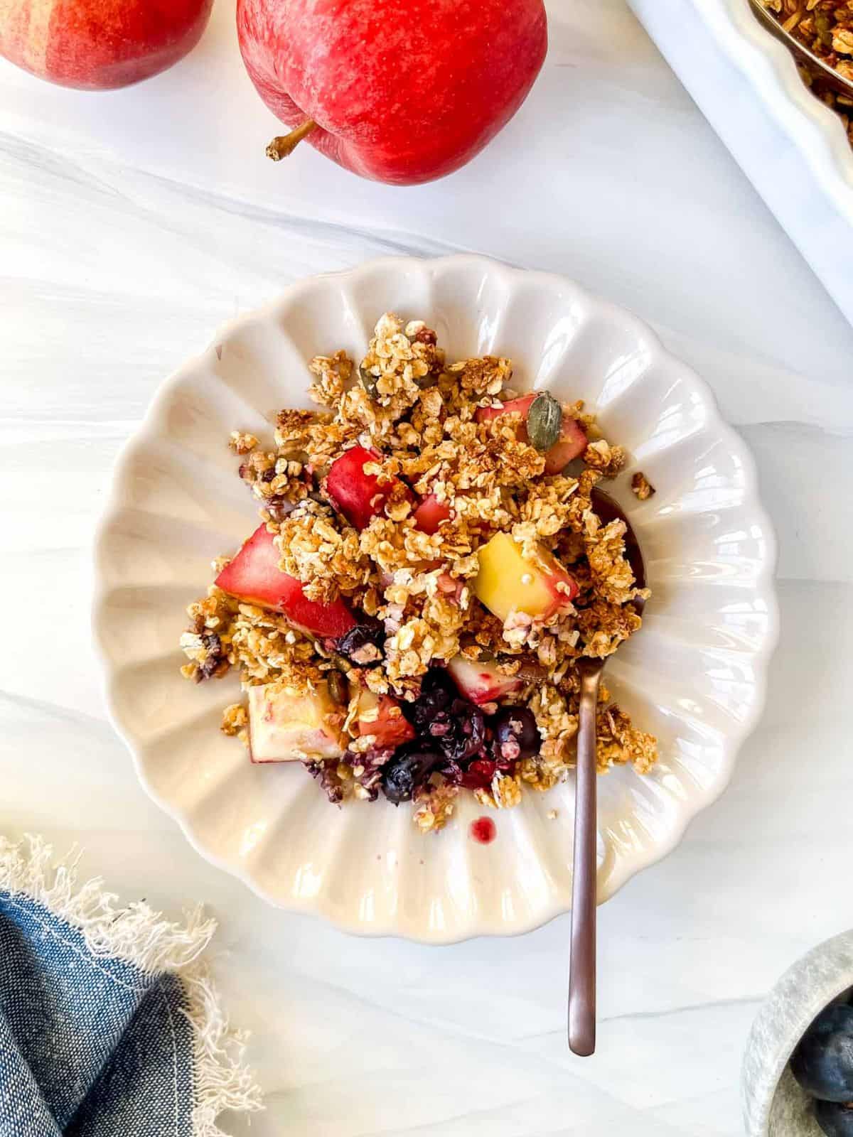 apple blueberry crisp on a cream plate with a spoon next to red apples.