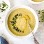 cauliflower potato leek soup in a white bowl with a spoon next to a small bowl of fresh thyme leaves.