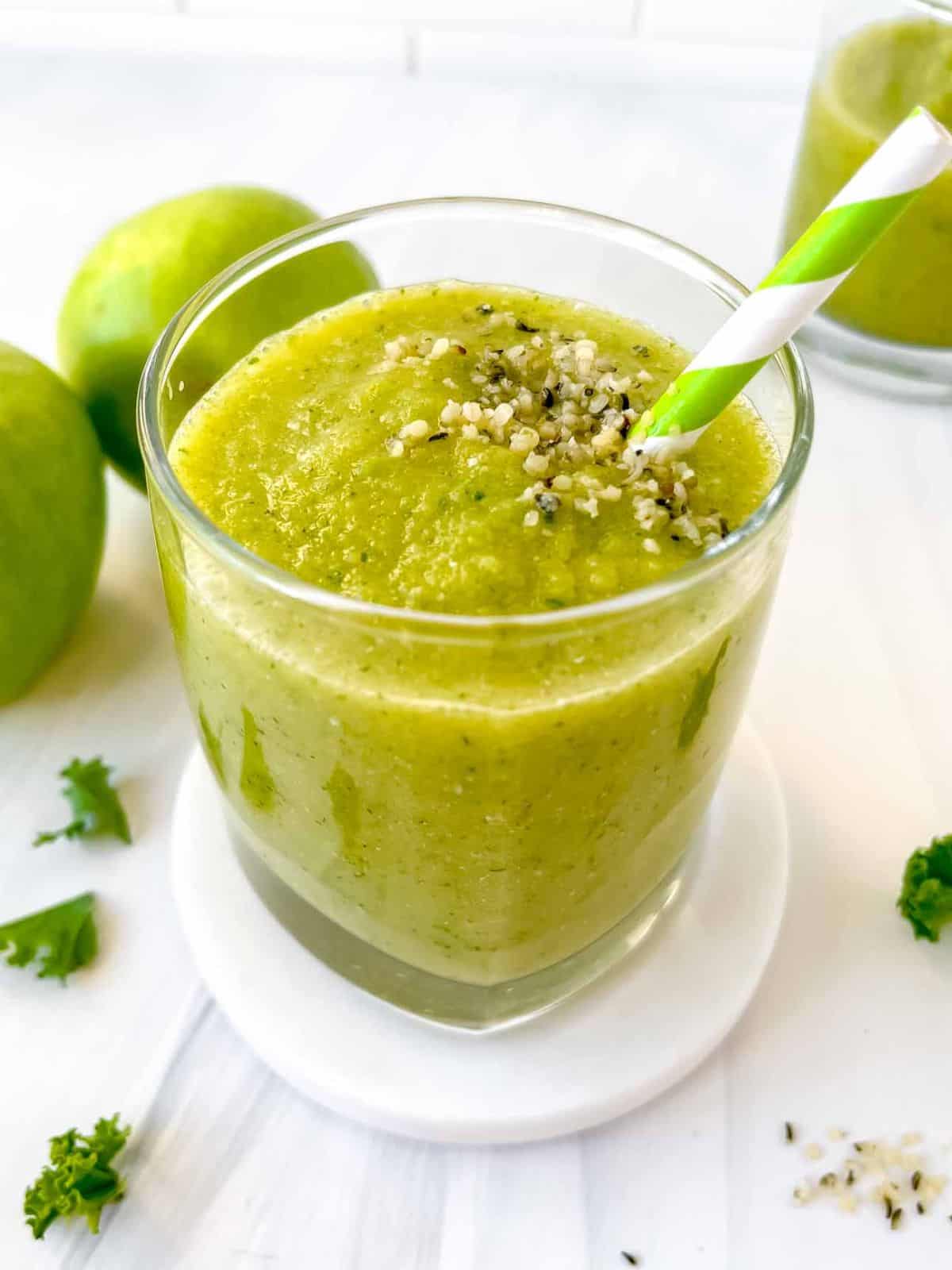 sour apple smoothie in a glass with a straw next to Granny Smith apples and kale leaves.