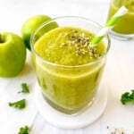 green apple smoothie in a glass next to Granny Smith apples and kale leaves.