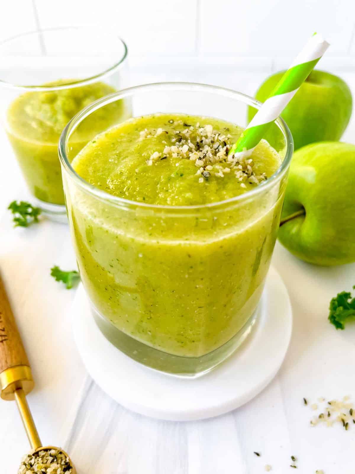 sour apple smoothie in two glasses next to green apples and a spoonful of hemp seeds.