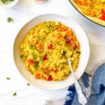 turmeric quinoa in a light grey bowl with a spoon next to a blue cloth.