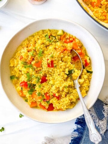 turmeric quinoa in a light grey bowl with a spoon next to a blue cloth.