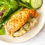 air fryer mozzarella stuffed chicken with salad leaves on a cream plate.