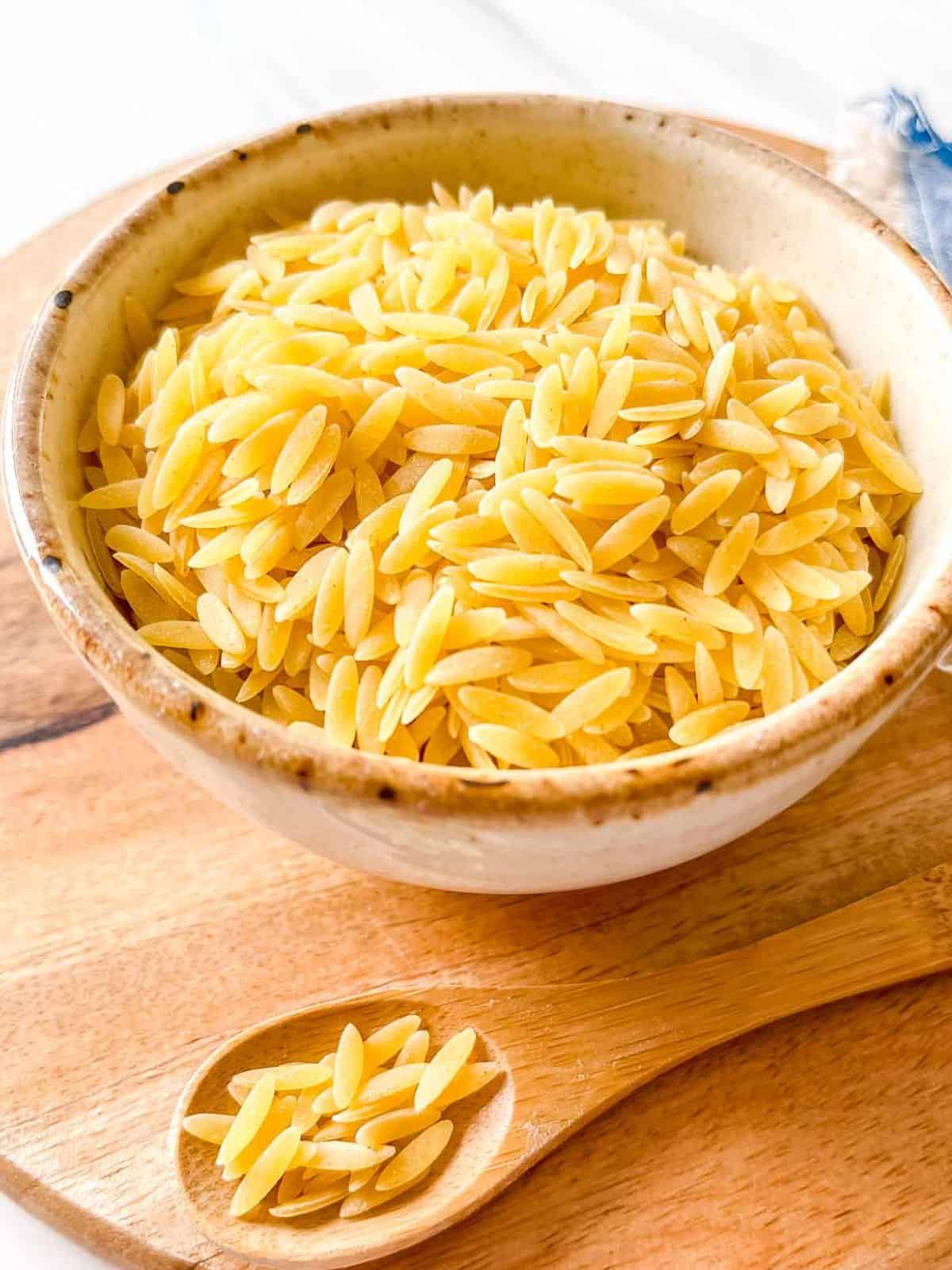 orzo pasta in a cream bowl and on a wooden spoon.