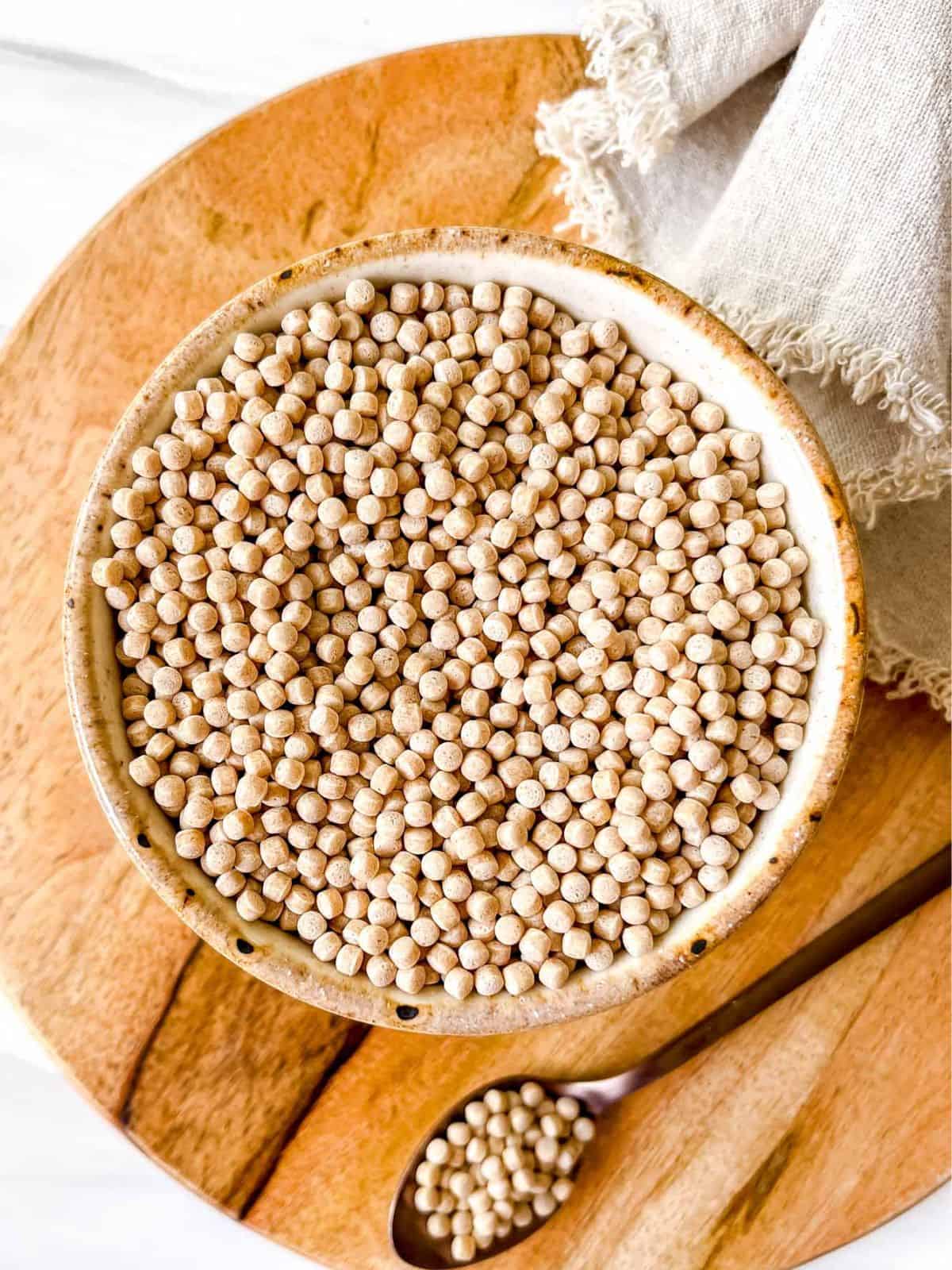 giant cous cous in a cream bowl on a wooden board.