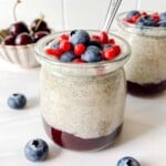 blended chia pudding topped with fruit in two glass jars with a bowl of cherries in the background.