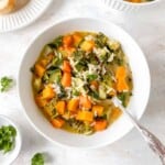 butternut squash wild rice soup in a white bowl with a spoon next to a bowl of fresh parsley.