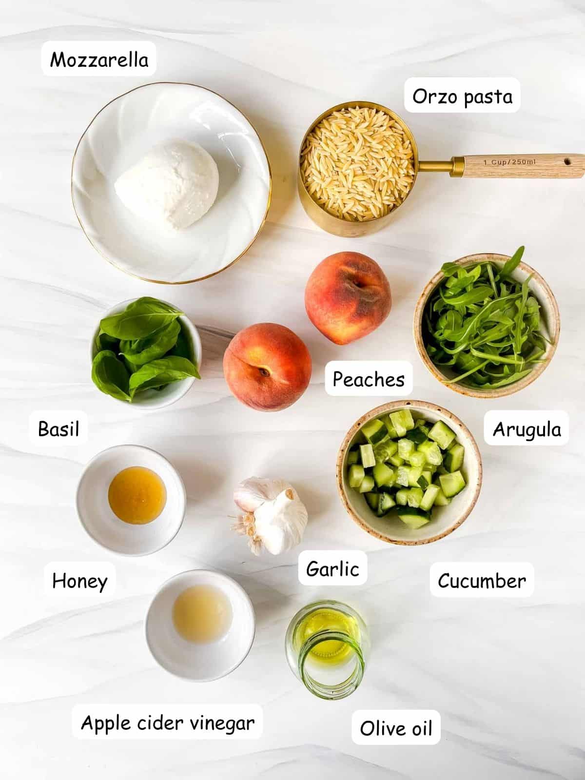 individually labelled ingredients to make peach pasta salad including arugula, mozzarella, cucumber, basil leaves and olive oil.