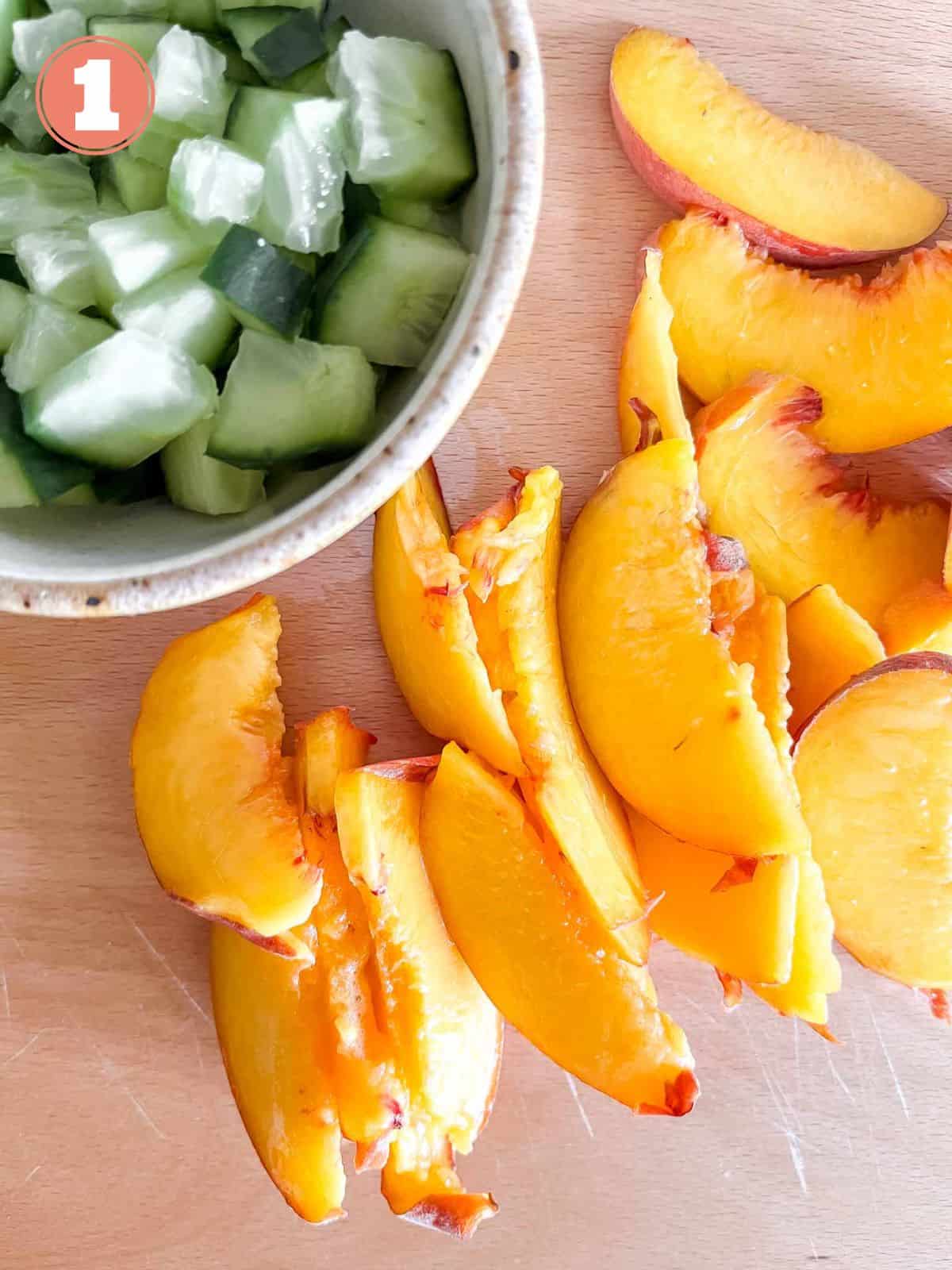 sliced peaches and bowl of diced English cucumber on a wooden chopping board labelled number one.