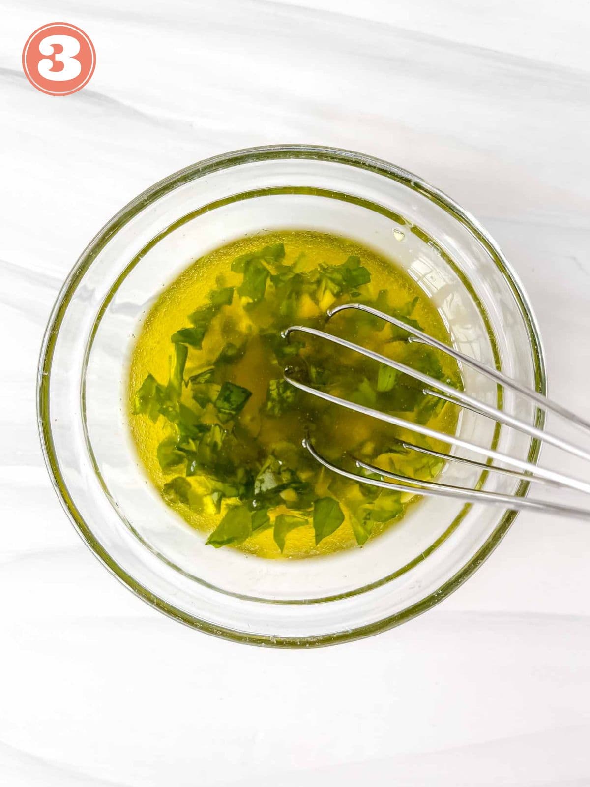 basil olive oil dressing in a glass bowl with a whisk labelled number three.