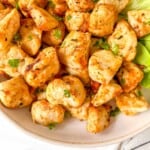 air fryer chicken bites without breading on lettuce on a cream plate.