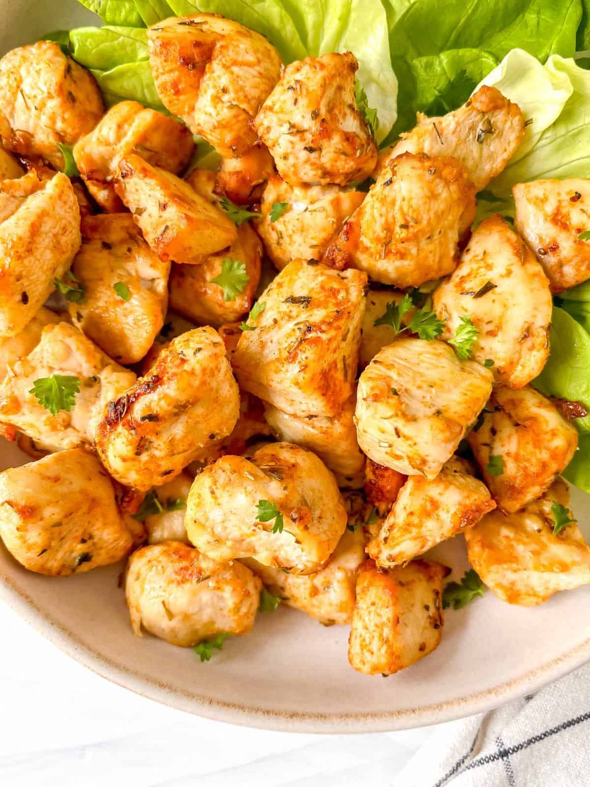 air fryer chicken bites without breading on lettuce on a cream plate.