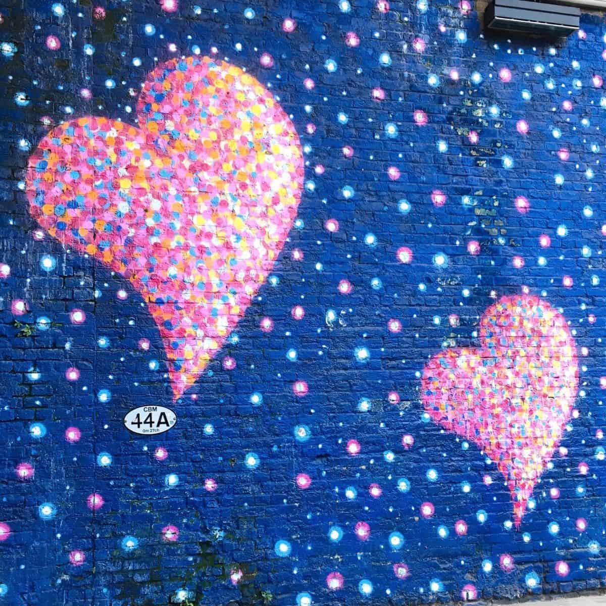 two pink hearts painted on a blue wall.