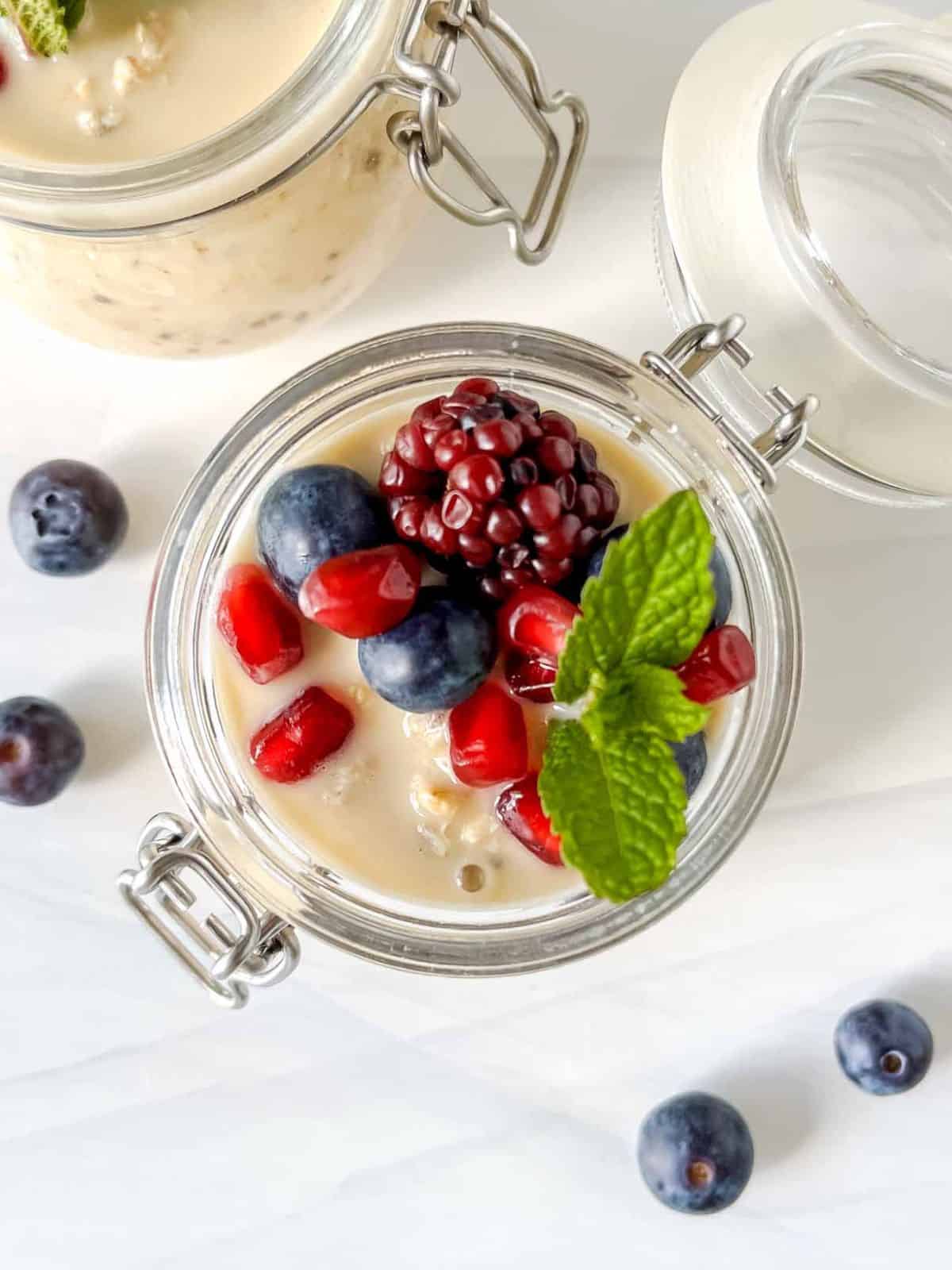 overnight oats with oat milk in two glass mason jars topped with fruit next to fresh blueberries.