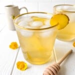 honey mocktail in two glasses next to yellow flowers and a honey dipper.