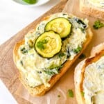 zucchini toast on a wooden board garnished with fresh herbs.