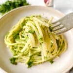 green pasta on a fork held over a bowl of pasta in green sauce.