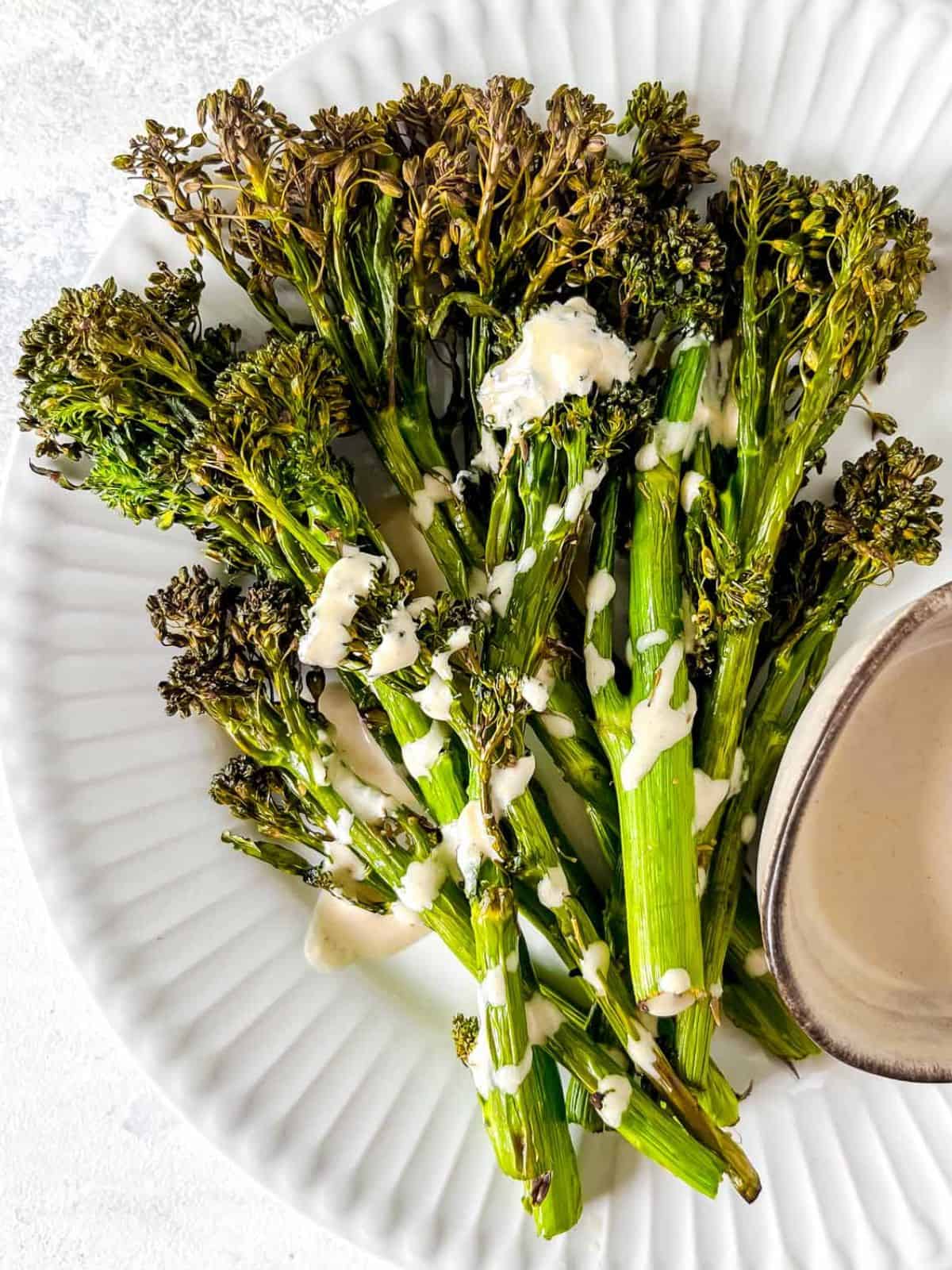 air fryer Tenderstem broccoli drizzled with tahini dressing on a white plate.