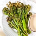 air fryer Tenderstem broccoli on a white plate with a small bowl of tahini dressing.