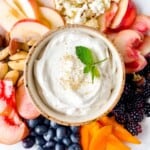 mascarpone dip for fruit in a bowl surrounded by fruits, berries and nuts.