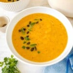 butternut leek soup in a white bowl topped with herbs and pumpkin seeds on a blue cloth.