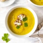 cauliflower zucchini soup in a white bowl topped with fresh parsley.