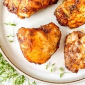 air fryer paprika chicken thighs on a beige plate with fresh herbs.