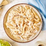 air fryer shredded chicken in a beige bowl next to forks and a blue cloth.