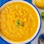 sweet potato and carrot soup in a white bowl with a blue rim next to a spoon.