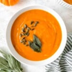 Hokkaido pumpkin in a white bowl next to fresh sage leaves and a striped cloth.