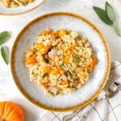 chicken pumpkin risotto in a grey bowl next to fresh sage leaves and a mini pumpkin.