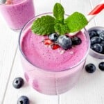 cottage cheese fruit smoothie in a glass garnished with fresh mint leaves and blueberries, next to a bowl of blueberries.