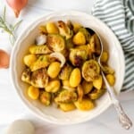 roasted gnocchi and Brussels sprouts in a white bowl with a spoon next to a green striped cloth and shallots.