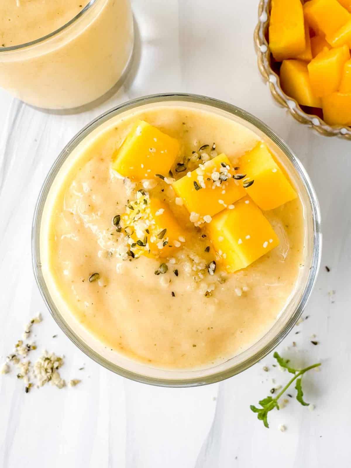 mango smoothie without banana in two glasses topped with fresh mango chunks.