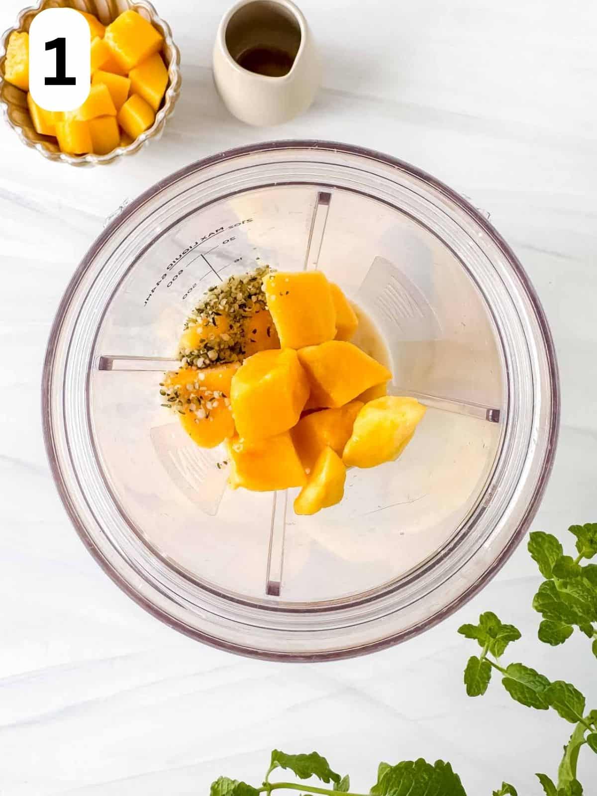 frozen mango chunks, hemp seeds and plant milk in a blender cup labelled number one.