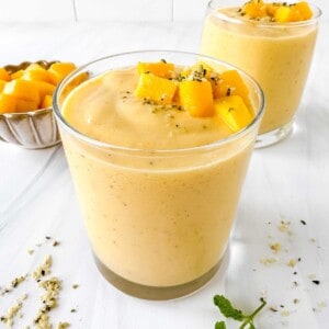 mango smoothie without banana in two glasses next to a small bowl of mango chunks.