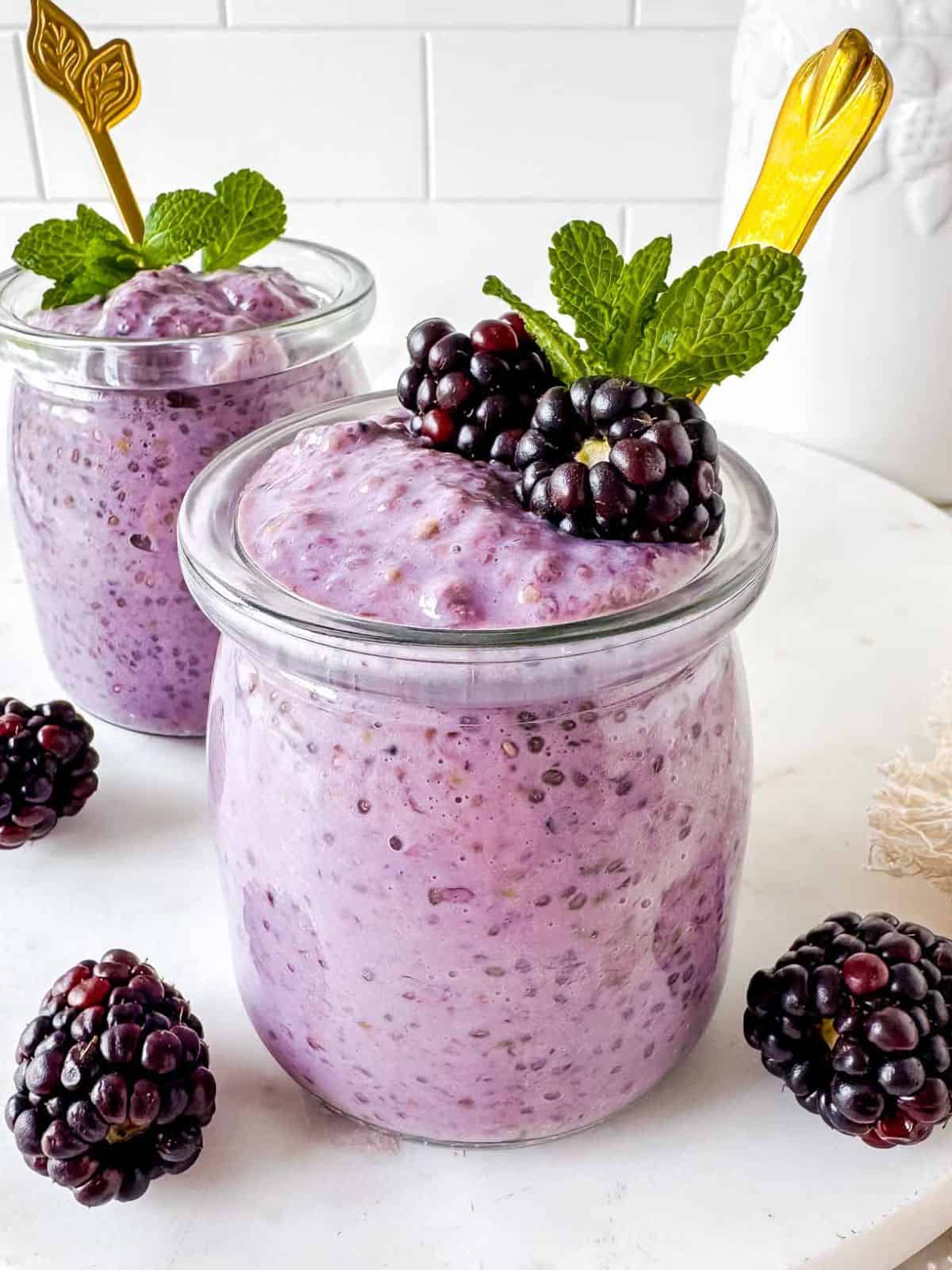 blackberry chia pudding in two glass jars topped with fresh blackberries and mint leaves.