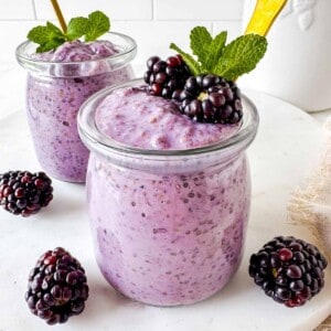 blackberry chia pudding in two glass jars topped with fresh blackberries and mint leaves.