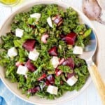 beet kale salad in a light brown bowl next to fresh beets and a bottle of olive oil.