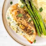 cottage cheese stuffed chicken breast with asparagus and mashed potatoes on a plate.