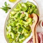 cucumber celery salad on a white plate next to fresh mint leaves and olive oil.