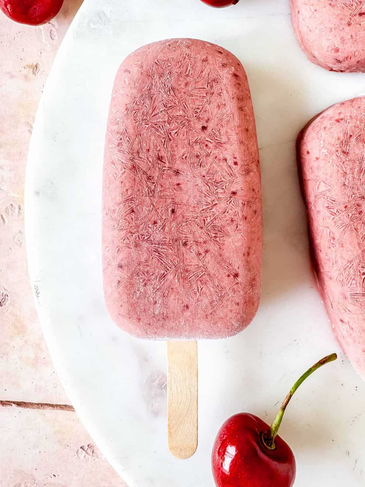 cherry coconut popsicles next to fresh cherries.