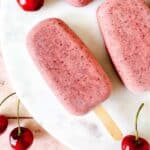 cherry coconut popsicles on a white background next to fresh cherries.